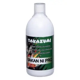 Biała butelka z zielono-czarną etykietą "TAKZUMI SAKAN NI PRO" z informacją o wsparciu i regeneracji ("BIJDRAGE OPWNNG EN HERSTEL UNTERSTÜTZUNG UND ERHOLUNG KEEP-UP AND RECOVERY"). Jest to płynny suplement lub środek wzmacniający dla ryb koi.